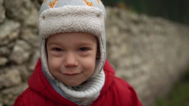 Close-up Retrato de pequeno menino pré-escolar europeu em cinza tricotado chapéu casaco vermelho triste, olhar ofendido para a câmera. Emocionalmente criança chateada preocupado posando lágrimas nos olhos olhando para a distância fora Outono — Vídeo de Stock