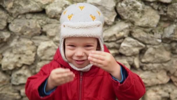 Close-up Retrato de menino pré-escolar europeu em cinza chapéu de malha casaco vermelho sorrindo olhar para a câmera. Emocionalmente criança rindo sorrindo posando olhos de cobertura com as mãos, ondas Olá fora Outono — Vídeo de Stock