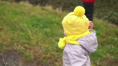 Bebek rünü. Gri tulumlu, sarı şapkalı küçük kız orman yolunda yürüyor. Çocuk komik bir aile hayali kuruyor. Yeni yürümeye başlayan çocuk dışarıda. neşeli mutlu çocukluk tasasız çocuklar bahçede yürür