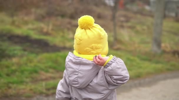 Детская рунада. Маленькая девочка в сером комбинезоне в жёлтой шляпе идёт по лесной дорожке. Малыш мечтает забавную семейную концепцию. Тоддлер снаружи. Весело счастливое детство беззаботных детей ходить ребенка во дворе — стоковое видео