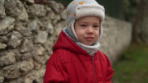 Zbliżenie Portret europejskiego małego przedszkolaka w szarej dzianinie czerwona kurtka smutna, obraźliwe spojrzenie w aparat fotograficzny. Emocjonalnie dziecko zdenerwowany stwarzając łzy w oczach patrząc w oddali poza jesienią — Wideo stockowe