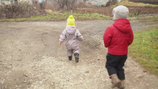 Bebé runing.Two niños pequeños en mono gris sombrero amarillo caminando a través del camino del parque forestal. niño sueño divertido concepto familiar. Hermanos afuera. diversión feliz infancia despreocupado niños niño niña caminar en el patio — Vídeo de stock