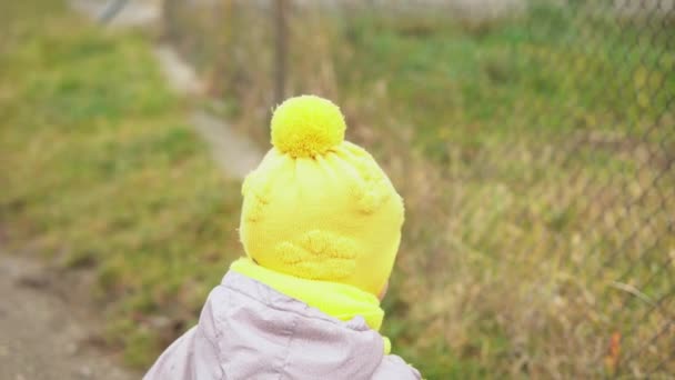 Dziecko rusza. Dziewczynka w szarym kombinezonie w żółtym kapeluszu spacerująca ścieżką leśnego parku. Dzieciak marzy o zabawnej rodzinie. Maluch na zewnątrz. zabawa szczęśliwy dzieciństwo beztroskie dzieci spacer dziecko w podwórku — Wideo stockowe