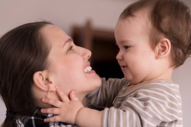 Sevimli küçük mutlu bebeğin sevimli yüzü. Sevimli gülüşü olan bebek bebek. Anneye bak. Anne kucaklaşması, evde sevgi öpücüğü ve gülümseyen kızı oynar.