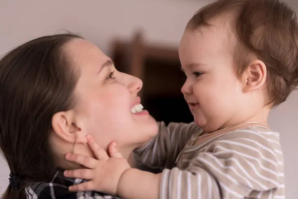 Retrato rosto adorável de pouco alegre criança bebê menina feliz com encantador sorriso olhar para a mãe forte abraços amando mamãe juntos. Mãe abraços jogar amor cuidado beijo sorrindo filha em casa — Fotografia de Stock