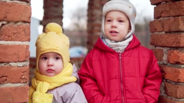 两个身穿灰色连衣裙、头戴黄色帽子的小孩穿过森林公园的小径。孩子梦到有趣的家庭观念。外面的兄弟们快乐快乐童年无忧无虑的小女孩在院子里散步 — 图库视频影像