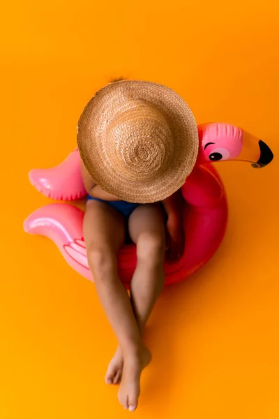 Glücklich kleines Kind Schwimmer Sport Baby-Mädchen tragen Sonnenstrohhut Badeanzug, Kid sitzen auf aufblasbaren Schwimmring rosa Flamingo, isoliert orange Hintergrund. Kindheit, heiße Sommerferien Hobby-Konzept — Stockfoto