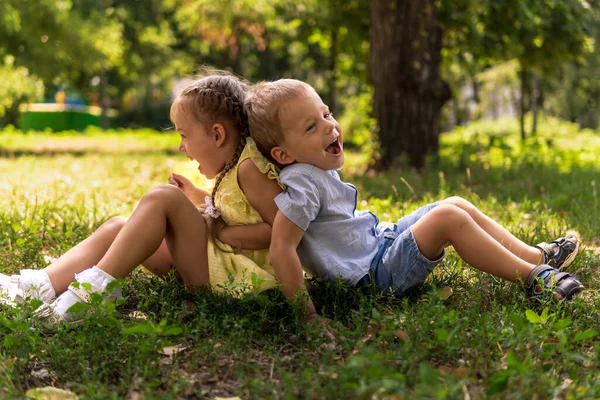 Dois felizes sorrindo alegre criança pré-escolar gêmeos irmãos crianças irmão irmã menino menina sentados juntos no gramado grama no parque em tempo de verão quente ensolarado. infância, amizade, conceito de família — Fotografia de Stock