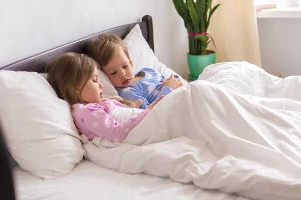 Kleine Vorschulkleinkind Kleinkinder Geschwister Kinder beobachten Cartoon verwenden Smartphone-Gerät zusammen. Baby im Pyjama auf weißem Bett zu Hause Schlafzimmer. Familie, Freizeit, Kindheit, Freundschaftskonzept — Stockfoto