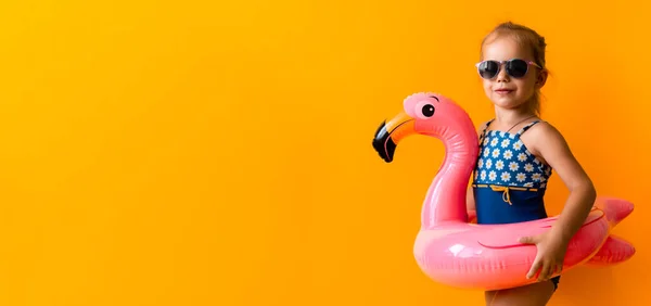 Banner šťastný malý dítě plavec sport dítě dívka nosit sluneční brýle plavky, Kid Nafukovací plavecký kroužek Pink Flamingo, izolované oranžové pozadí, horké letní prázdniny hobby koncept. Kopírovat mezeru — Stock fotografie