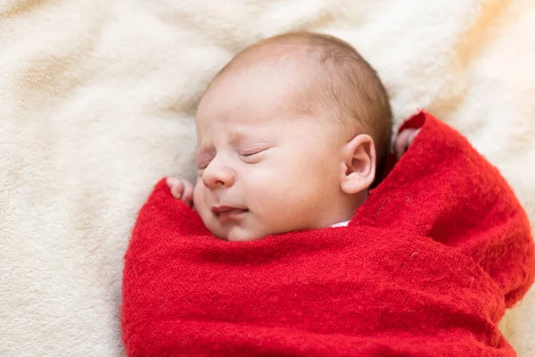 Top View Portrait First Days of Life Bayi yang baru lahir Bayi yang tertidur di Santa Hat Wrapped Di Karpet Kertas Merah Di Latar Belakang White Garland. Selamat Natal, Selamat Tahun Baru, Bayi, Masa kecil, Konsep Musim Dingin Stok Gambar