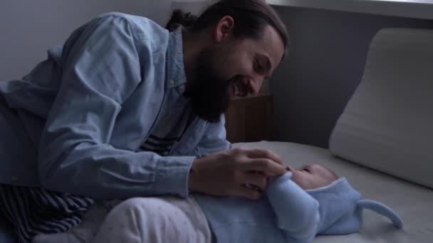 Autentiske skæg langhåret ung neo far og nyfødt baby ser hinanden smilende på sengen. Far lå med spædbarn. Børn, Forældreskab, Barndom, Liv, Kærlighed, Faderskab, Familiekoncept – Stock-video