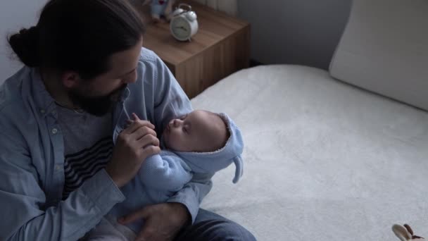 Tournage cinématographique barbu jeune néo-père aux cheveux longs tient et embrasser la main du nouveau-né à la maison. Papa tenant un nourrisson. Amour, Enfants, Paternité, Vie, Paternité, Concept familial, Paternité — Video