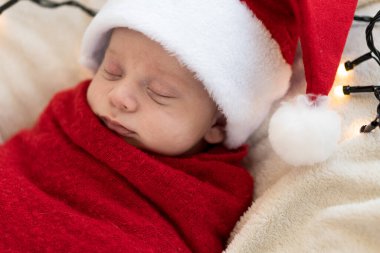 Yeni doğanların ilk portresi. Beyaz çelenk arka planında kırmızı beze sarılı, tatlı, uyuyan, Noel Baba şapkalı bebek. Mutlu Noeller, Mutlu yıllar, Bebek, Çocukluk, Kış
