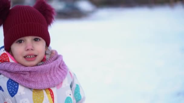 Close up Portrait Little Child Pretty Girl Kid Smiling Looking at Camera posing in red hat coughing Snow Park Outdoor. Winter time, happiness concept. Snowing Cold frosty weather. Carefree childhood — Wideo stockowe