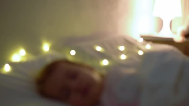 Söt Chuby Little Toddler Baby Girl 1-2 år gammal sovande i rosa Pajama på vit säng i mörkt sovrum. Barn har koppla av vilotid på natten Garland på kudde. Barndom, Jul, Föräldraskap Begreppet — Stockvideo