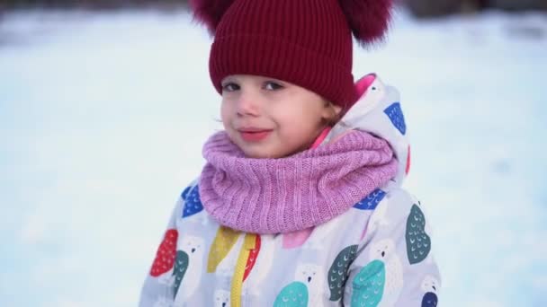 Close up Portrait Little Child Pretty Girl Kid Smiling Looking at Camera posing in red hat coughing Snow Park Outdoor. Winter time, happiness concept. Snowing Cold frosty weather. Carefree childhood — Wideo stockowe