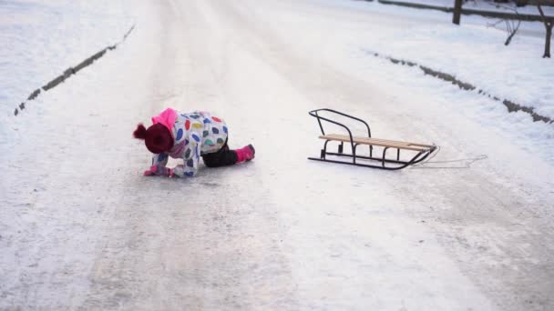 Menina pré-escolar branca engraçada pequena feliz no revestimento colorido com a queda do trenó na neve no inverno. Crianças bonitos são Sledding. Bebê andando na estrada nevada ou caminho. Infância, Transporte, Conceito de férias — Vídeo de Stock