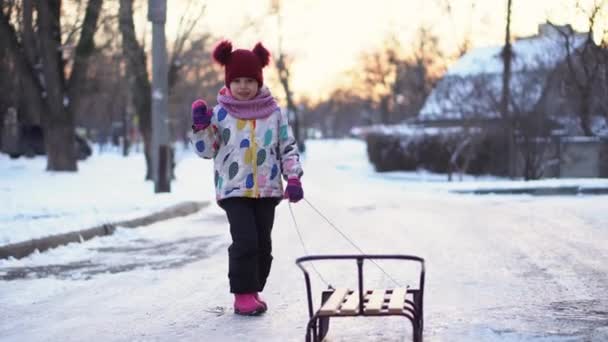 Happy Little Funny White Preschool Girl en chaqueta colorida con trineo que agita la mano en invierno de nieve. Los niños van en trineo. Bebé caminando en camino nevado o camino. Infancia, Transporte, Concepto de vacaciones — Vídeos de Stock