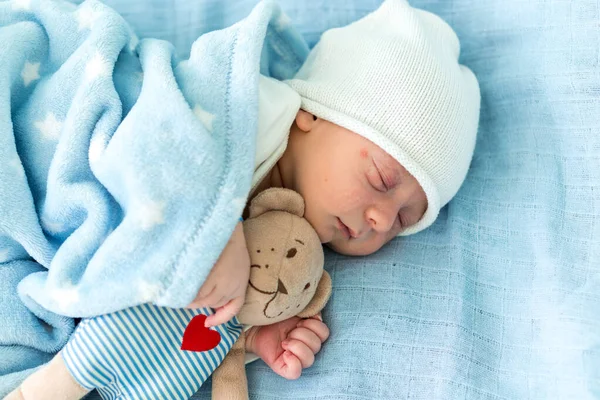 Close-up van pasgeboren baby gezicht portret vroege dagen slapen met Tady Bear op blauwe achtergrond. Kind aan het begin Minuten van het leven op hoed. Zuigelingen, Bevalling, Eerste momenten van Borning, Beginnen Concept. — Stockfoto