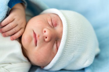 Yeni doğan bebek kırmızı şirin surat portresi. Eski günlerde mavi arka planda, cam yatakta uyuyordu. Hayatın başlangıcındaki çocuk şapkayla. Bebekler, Doğum, Doğumun İlk Anları, Başlangıç Konsepti