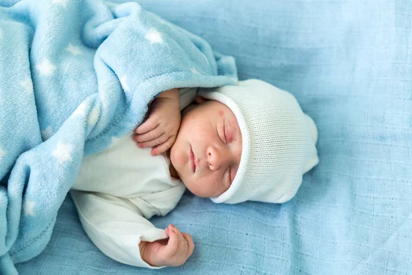 Retrato de rosto bonito vermelho do bebê recém-nascido primeiros dias dormindo na cama de vidro médico no fundo azul. Criança no início minutos de vida no chapéu. Bebês, Parto, Primeiros Momentos de Borning, Princípio de Início — Fotografia de Stock