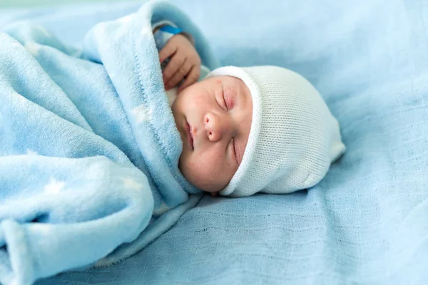 Retrato de rosto bonito vermelho do bebê recém-nascido primeiros dias dormindo na cama de vidro médico no fundo azul. Criança no início minutos de vida no chapéu. Bebês, Parto, Primeiros Momentos de Borning, Princípio de Início — Fotografia de Stock