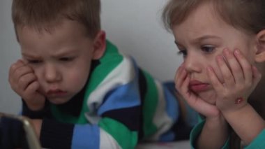 Otantik 3 küçük anaokulu çocuğu reşit olmayan çocuklar, kardeşler akıllı telefon cihazıyla çizgi film izliyorlar evde beyaz yatakta bebek gibi. Aile, eğlence, çocukluk, arkadaşlık konsepti..