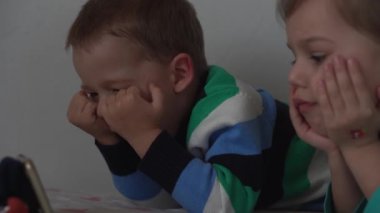 Otantik 3 küçük anaokulu çocuğu reşit olmayan çocuklar, kardeşler akıllı telefon cihazıyla çizgi film izliyorlar evde beyaz yatakta bebek gibi. Aile, eğlence, çocukluk, arkadaşlık konsepti..