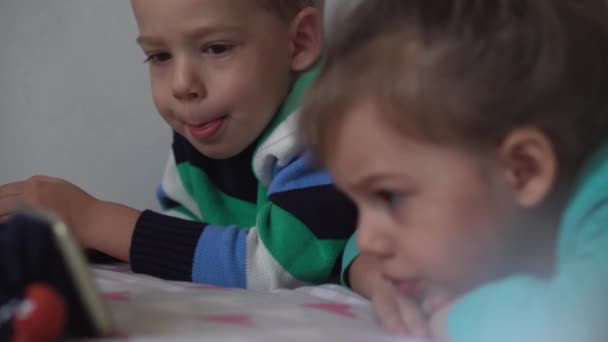 Autentyczne 3 małe przedszkolaki dzieci rodzeństwo dzieci oglądać kreskówkę na smartfonie urządzenie razem dziecko na białym łóżku w domu w domu. Rodzina, czas wolny, dzieciństwo, koncepcja przyjaźni. — Wideo stockowe