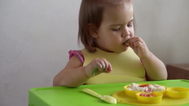 Primer plano de niña encantadora comiendo desayunar huevos verduras salchicha por sí misma en casa. Adorable niño feliz positivo come con la cara sucia en el interior de la mesa. Alimentación, nutrición una vida sana — Vídeos de Stock