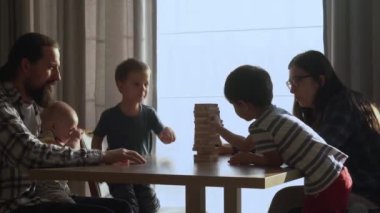 Küçük Çocuklar Masada ailesiyle küçük Jenga oynuyorlar, Jenga Kulesi dağılıyor, Aileler evde harika vakit geçiriyorlar Güneşli odada oyun oynuyorlar, Mutlu çocukluk, Arkadaşlık konsepti