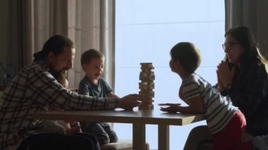 Küçük Çocuklar Masada ailesiyle küçük Jenga oynuyorlar, Jenga Kulesi dağılıyor, Aileler evde harika vakit geçiriyorlar Güneşli odada oyun oynuyorlar, Mutlu çocukluk, Arkadaşlık konsepti