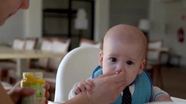 Anne beyazı besler, yüksek sandalyeyi besler, ilk sebze püresi yapar mutlu, gülümseyen çocuk ilk kez yer, kirli yüzlü çocuk, yulaf lapası yer.