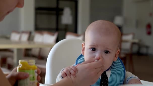 Mamma mamma alimenta il bambino in bianco nutrendosi del seggiolone, primo integratore di purea vegetale Buon bambino sorridente mangia per la prima volta, bambino con la faccia sporca, bambino piccolo che mangia porridge nutrizione — Video Stock