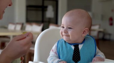 Anne beyazı besler, yüksek sandalyeyi besler, ilk sebze püresi yapar mutlu, gülümseyen çocuk ilk kez yer, kirli yüzlü çocuk, yulaf lapası yer.