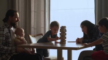 Küçük Çocuklar Masada ailesiyle küçük Jenga oynuyorlar, Jenga Kulesi dağılıyor, Aileler evde harika vakit geçiriyorlar Güneşli odada oyun oynuyorlar, Mutlu çocukluk, Arkadaşlık konsepti