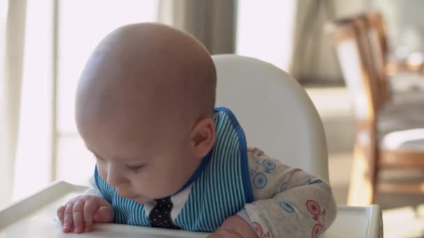 Enfance, bonheur, famille, altérité. Joyeux bébé souriant joyeux Gros plan visage. Les émotions du nouveau-né. enfant dans un bavoir assis dans une chaise d'alimentation grignote cure-dent dans la cuisine, douleur de gencive infantile — Video