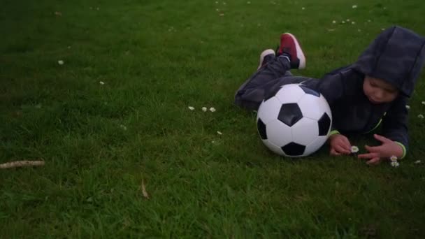 Bonne famille d'enfants qui s'amusent à Spring Park. Little Kid Run. Enfant garçon couché avec noir blanc ballon de football classique sur herbe verte. Les gens jouent au football. Enfance, Sport, Championnat Concept — Video