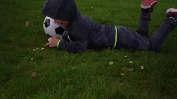 Bonne famille d'enfants qui s'amusent à Spring Park. Little Kid Run. Enfant garçon couché avec noir blanc ballon de football classique sur herbe verte. Les gens jouent au football. Enfance, Sport, Championnat Concept — Video