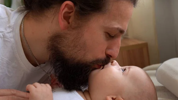 Homem Barbudo Jovem Autêntico Segurando Bebê Recém-nascido. Pai e filho na cama. Close-up Retrato de família sorridente com o bebê nas mãos. Casamento feliz Casal no fundo. Infância, Conceito de paternidade — Fotografia de Stock