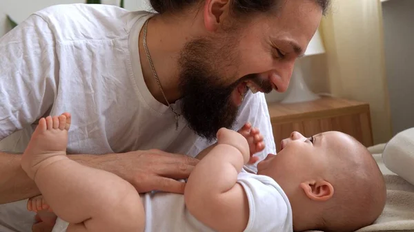 Homem Barbudo Jovem Autêntico Segurando Bebê Recém-nascido. Pai e filho na cama. Close-up Retrato de família sorridente com o bebê nas mãos. Casamento feliz Casal no fundo. Infância, Conceito de paternidade — Fotografia de Stock