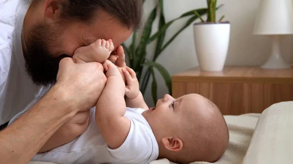 Homem Barbudo Jovem Autêntico Segurando Bebê Recém-nascido. Pai e filho na cama. Close-up Retrato de família sorridente com o bebê nas mãos. Casamento feliz Casal no fundo. Infância, Conceito de paternidade — Fotografia de Stock