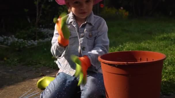 Щаслива дівчинка дошкільного віку маленька дівчинка Дочка носить робочі рукавички гумінові чоботи, висаджуючи квіти в горщику в саду. Дитина допомагає матері. Сімейна природа сміття, екологічна концепція весняного літа — стокове відео