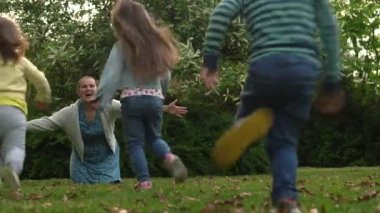 Happy family mother, two Three little siblings kids playing running hug kiss mom enjoying summer holidays in garden or park. Smiling parents children are spending leisure time together evening sunset