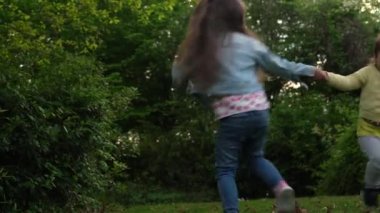 Friends Excited young children siblings Dancing have fun on grass meadow. Little two sisters spinning by the hands kissing. Family siblings play together outside in park garden summer holidays