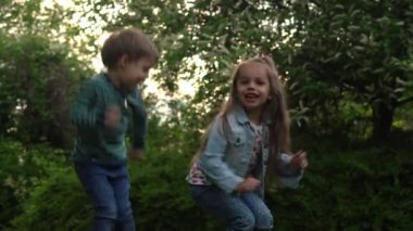 Friends Excited young children siblings Dancing have fun on grass meadow. Little brother and sister monkeying on camera kissing. Family siblings play together outside in park garden summer holidays