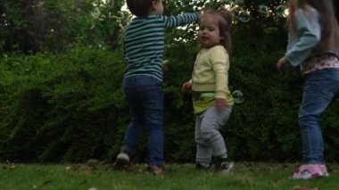 Mutlu bir aile annesi, iki küçük kardeş çocuk sabun köpüğü üflüyor ve yaz tatillerinin tadını çıkarıyorlar. Gülümseyen ebeveynler çocuklar akşam günbatımında birlikte vakit geçiriyorlar.