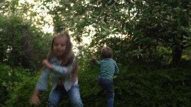 Friends Excited young children siblings Dancing have fun on grass meadow. Little brother and sister monkeying on camera kissing. Family siblings play together outside in park garden summer holidays