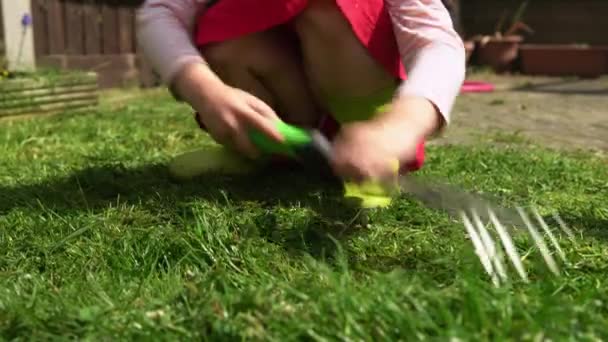 Zavlažování zahradních rostlin. Dítě nosit deštivé boty pomáhají hrabat zelené trávníku trávníku pozemek rostlin ve slunečný den Venku. Dcera se stará o květiny Pomáhá matce s domem. Rodina, Dětství, Příroda — Stock video